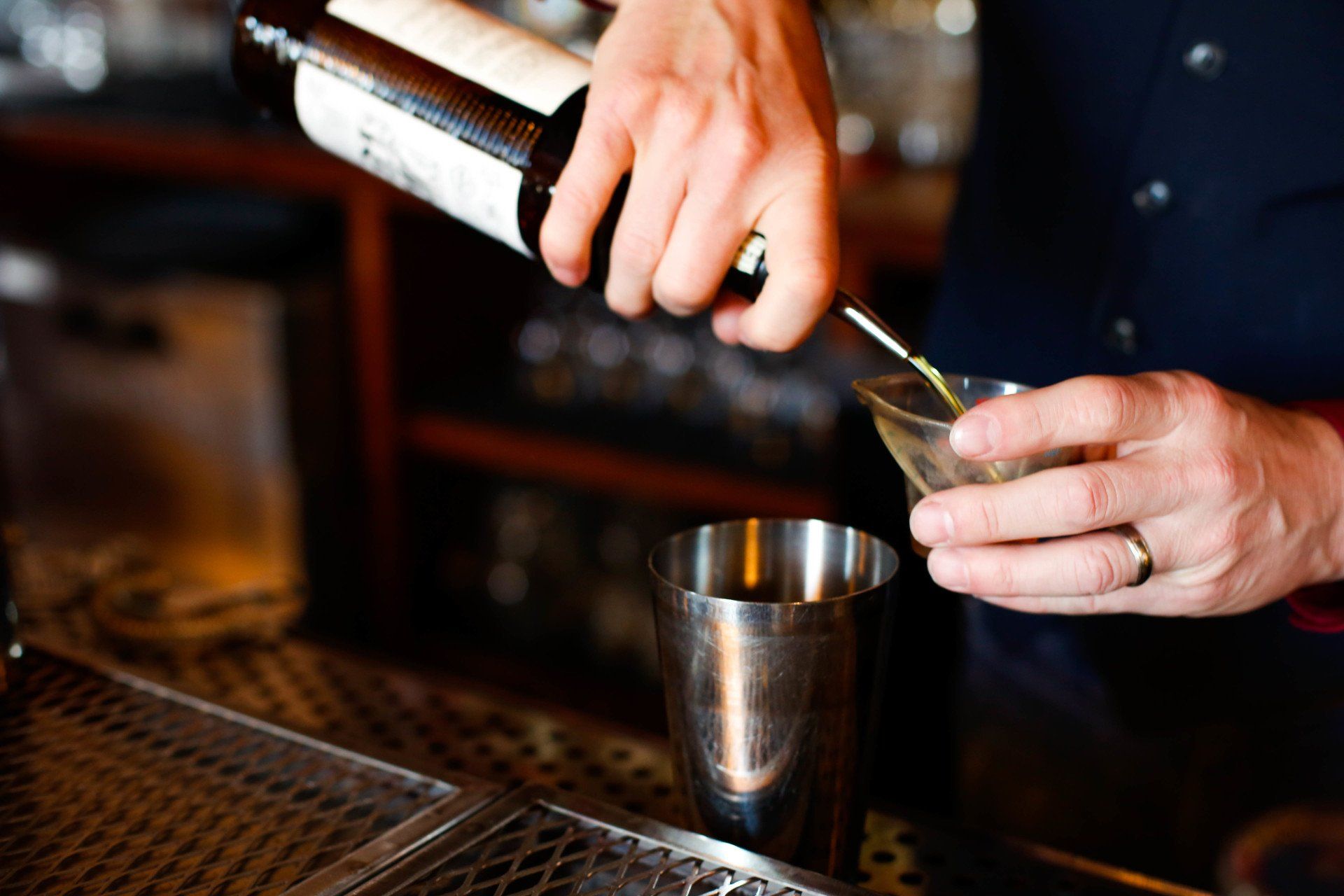 close up of bartenders hands measuring out liquor to pour into metal cocktail mixer
