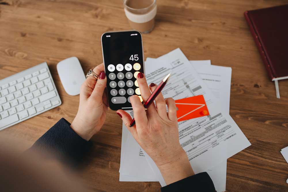 A woman is using a calculator and a pen while sitting at a desk.