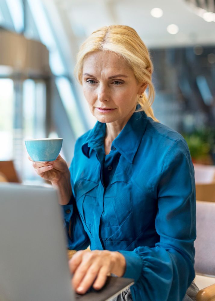 A woman is holding a cup of coffee while using a laptop computer.