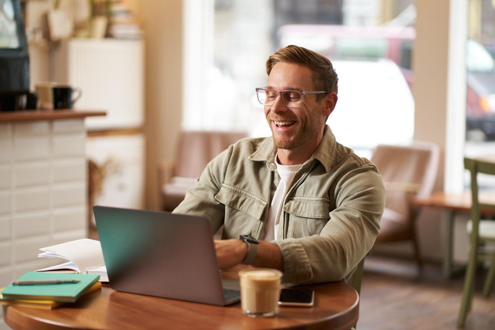 A man is sitting at a table using a laptop computer.