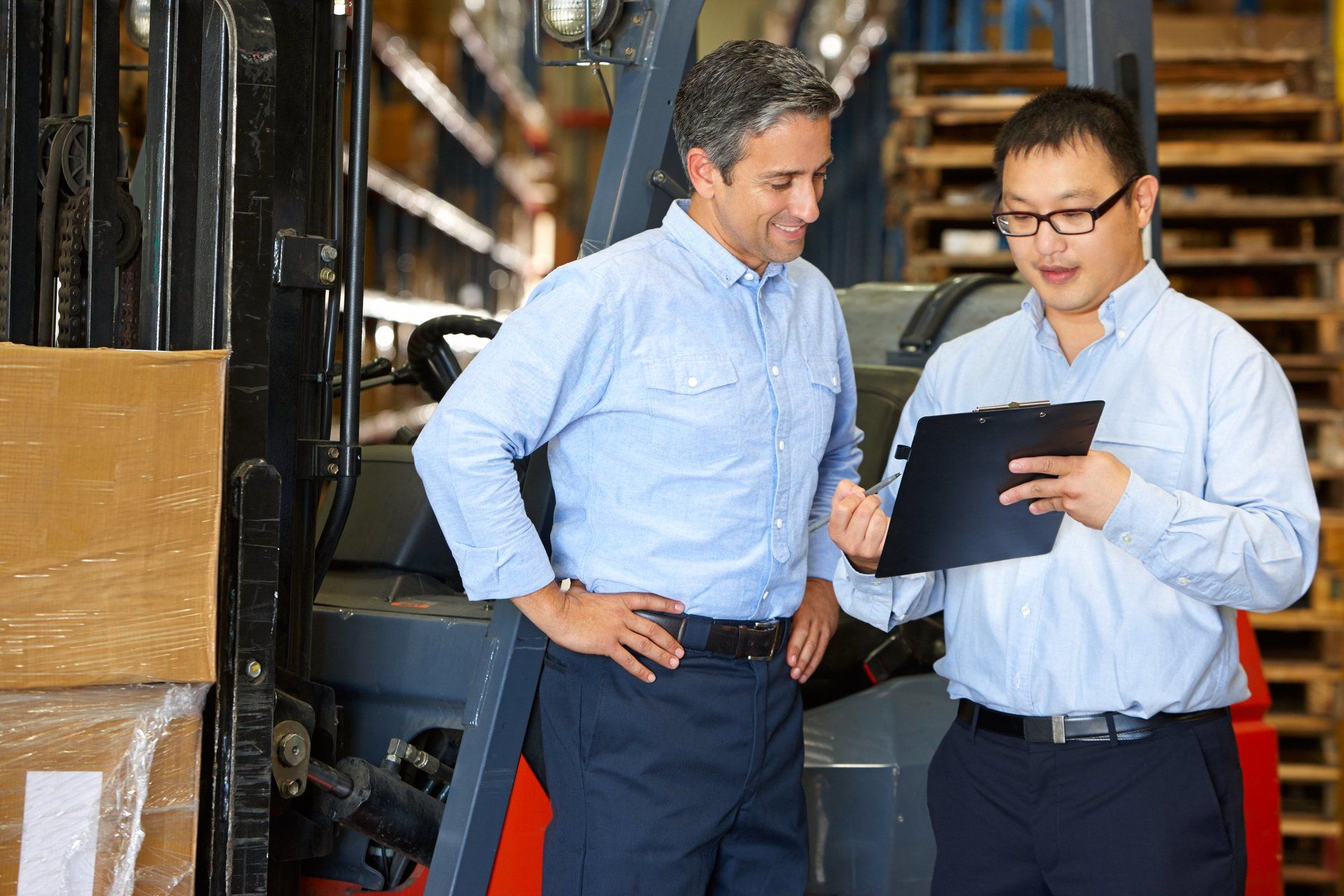 Two men are standing next to each other in a warehouse looking at a clipboard.