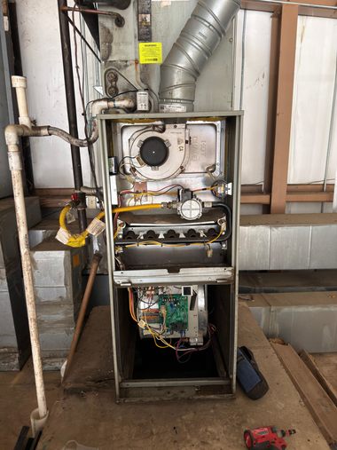Open furnace cabinet with exposed ducts and wiring in a utility room, front panel removed.