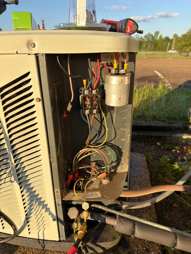 Open electrical panel on an outdoor HVAC unit with exposed wiring and components