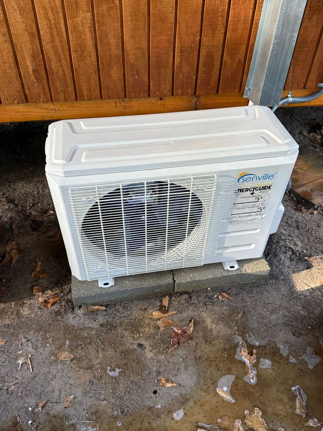 White outdoor air conditioner unit on a concrete pad beside a wooden fence.