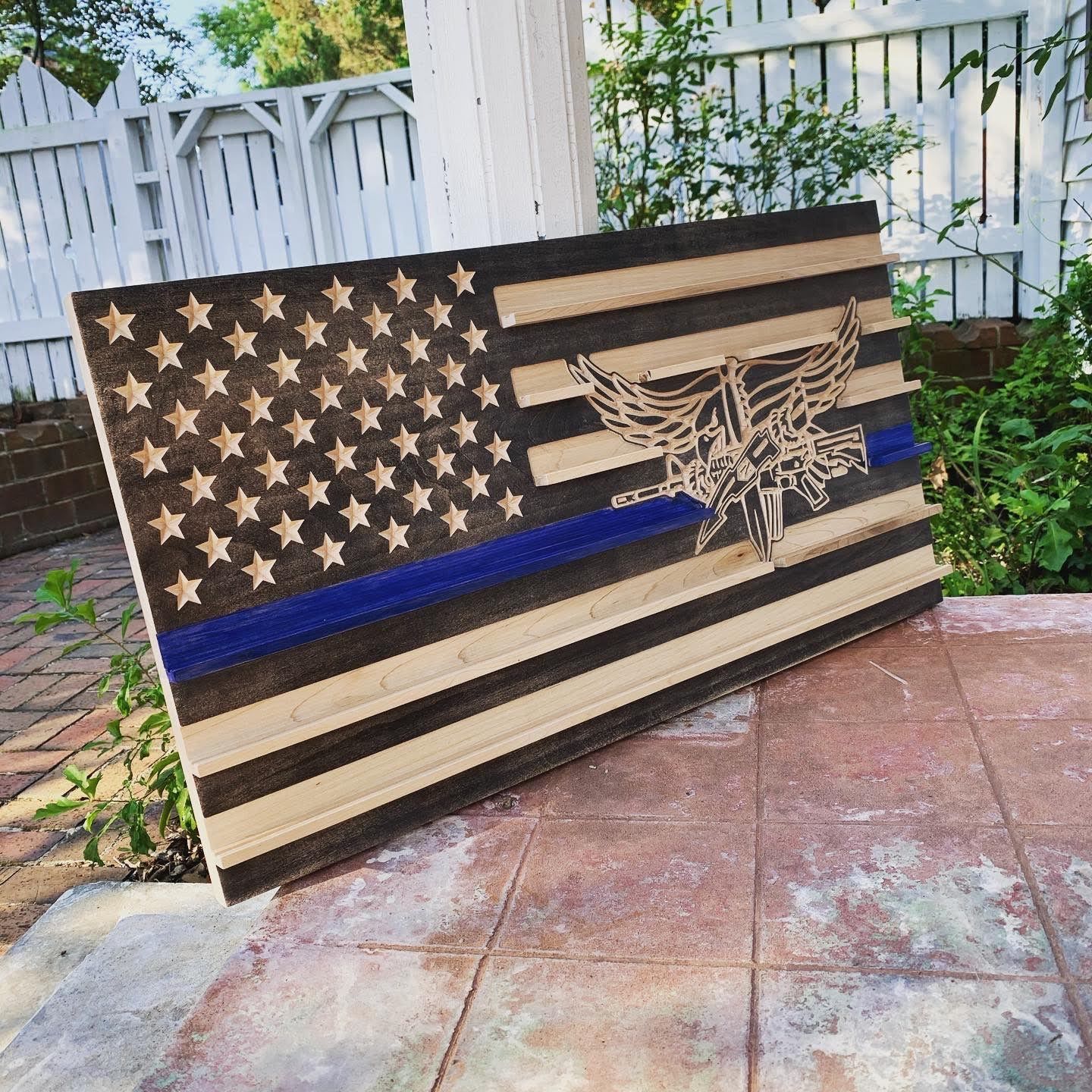 A wooden american flag with a blue line and an eagle on it is sitting on a tiled floor.