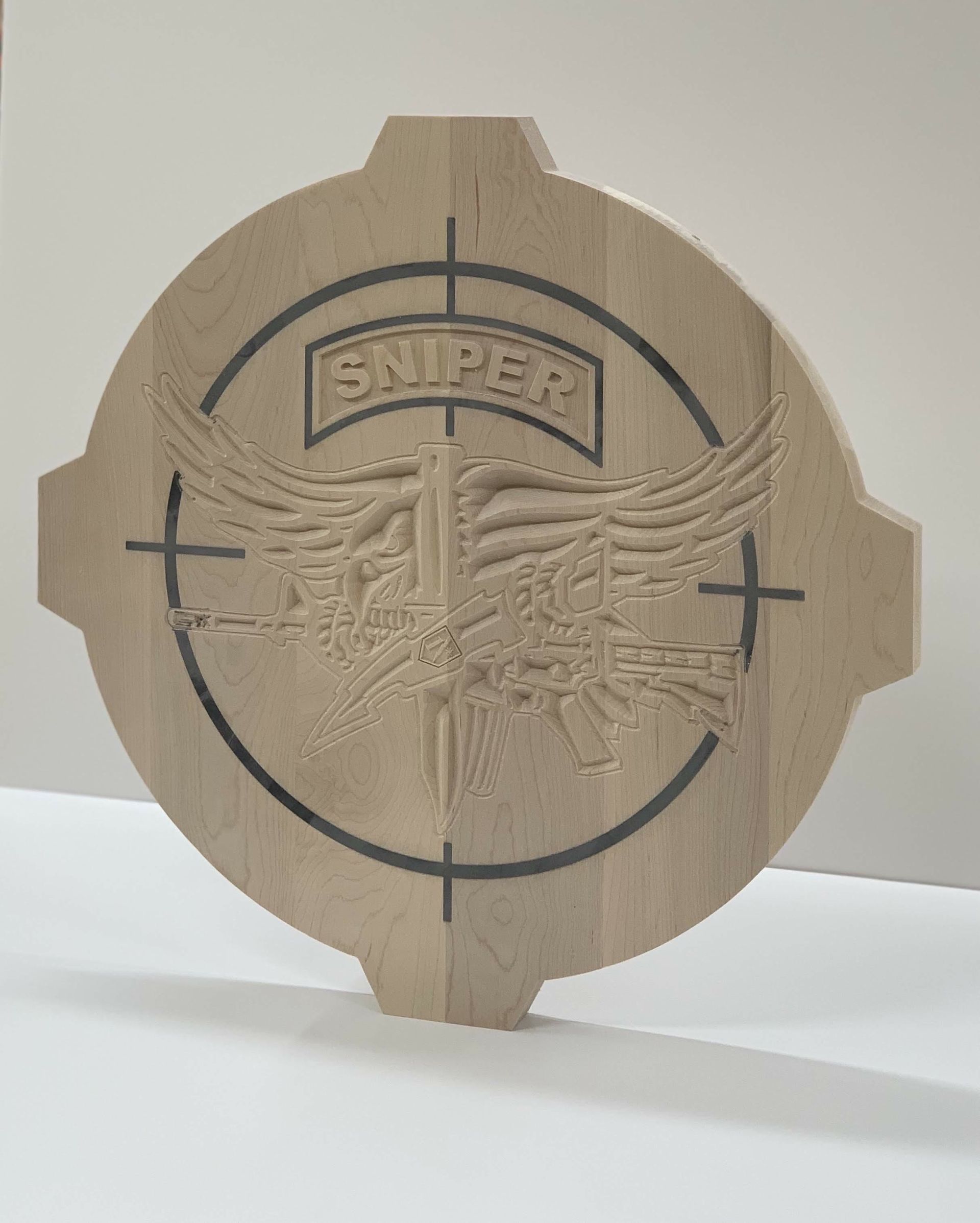 A sniper logo is carved into a piece of wood