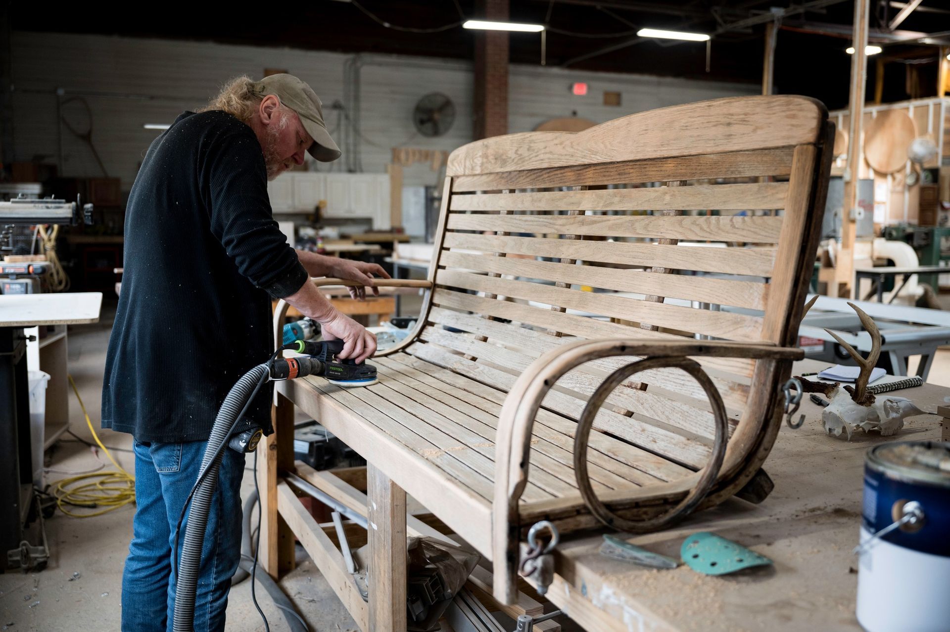 A man is sanding a wooden bench in a workshop.
