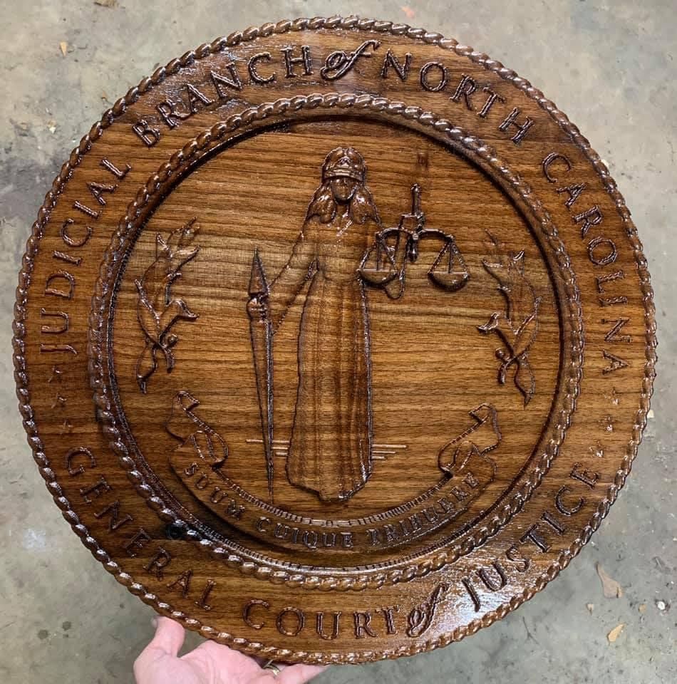 A person is holding a wooden seal for the judicial branch of north carolina