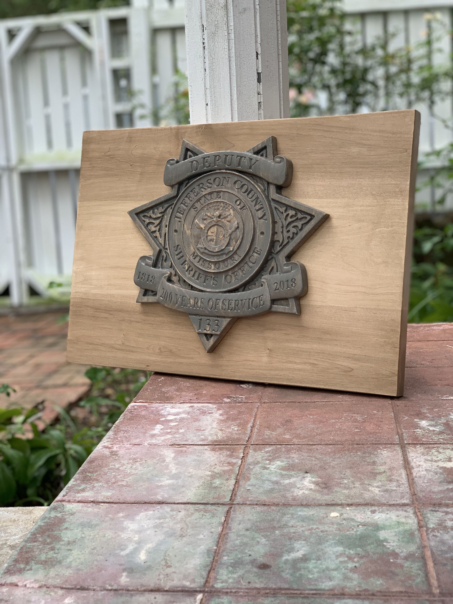 A wooden plaque with a badge on it is sitting on a brick sidewalk.