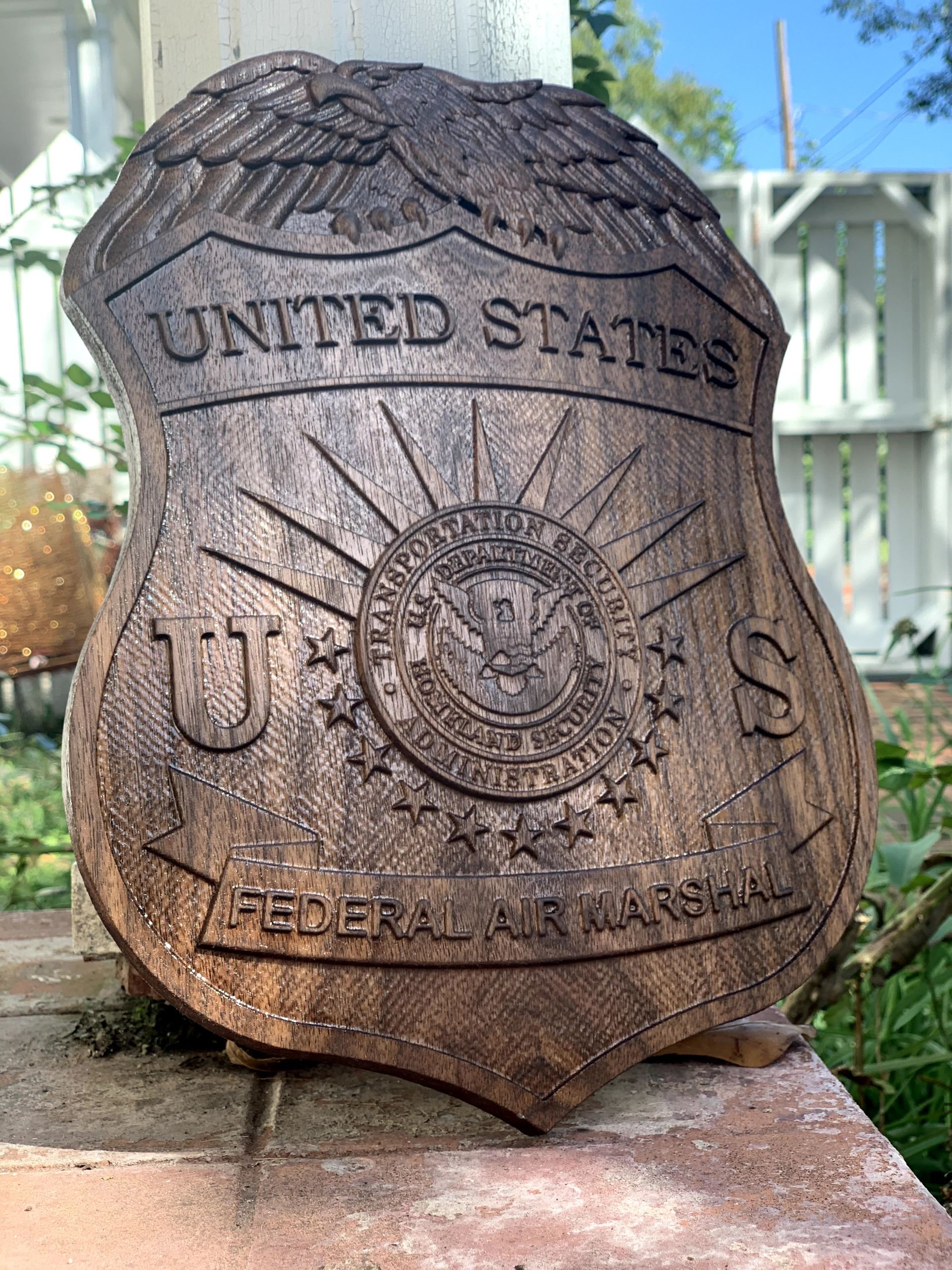 A wooden united states federal air marshal badge is sitting on a brick wall.