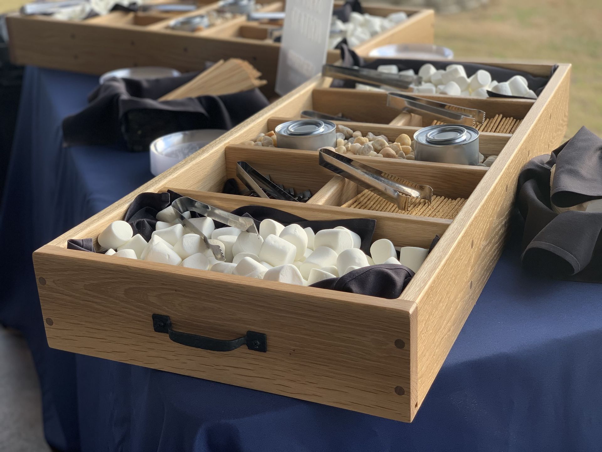 A wooden tray filled with marshmallows and tongs on a table.