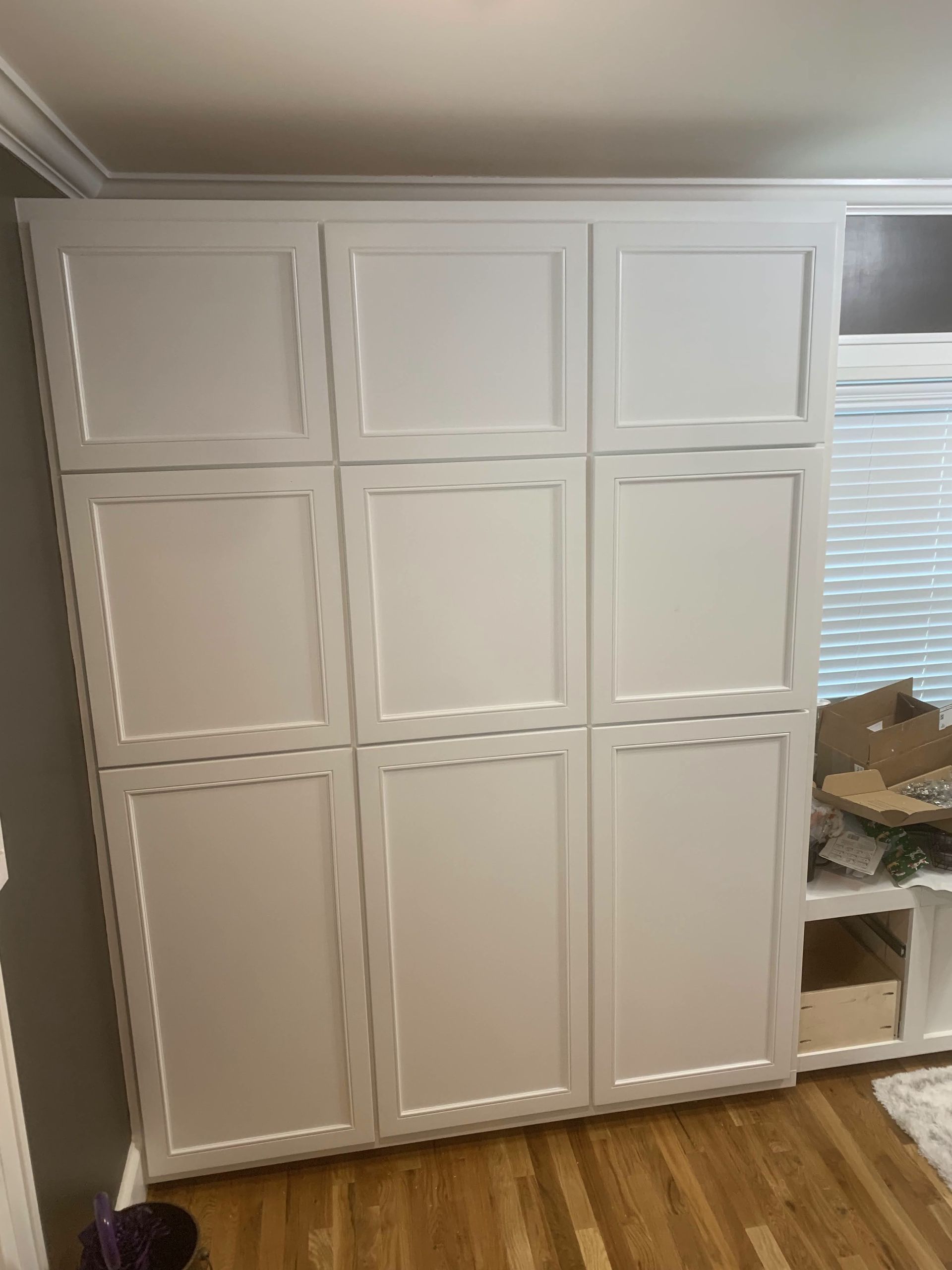 A white cabinet is sitting on a wooden floor in a room next to a window.