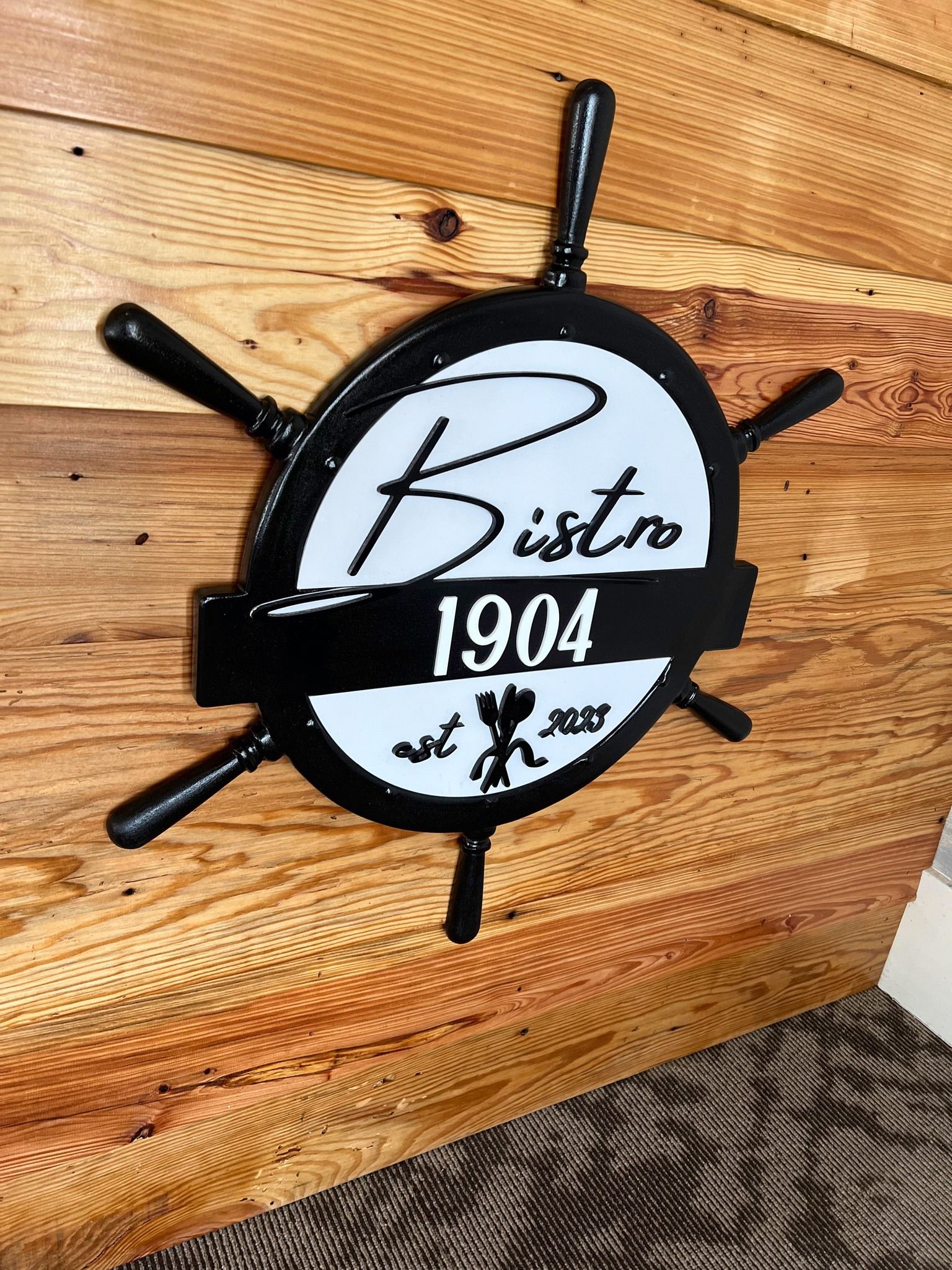 A wooden sign with a steering wheel on it is on a wooden table.