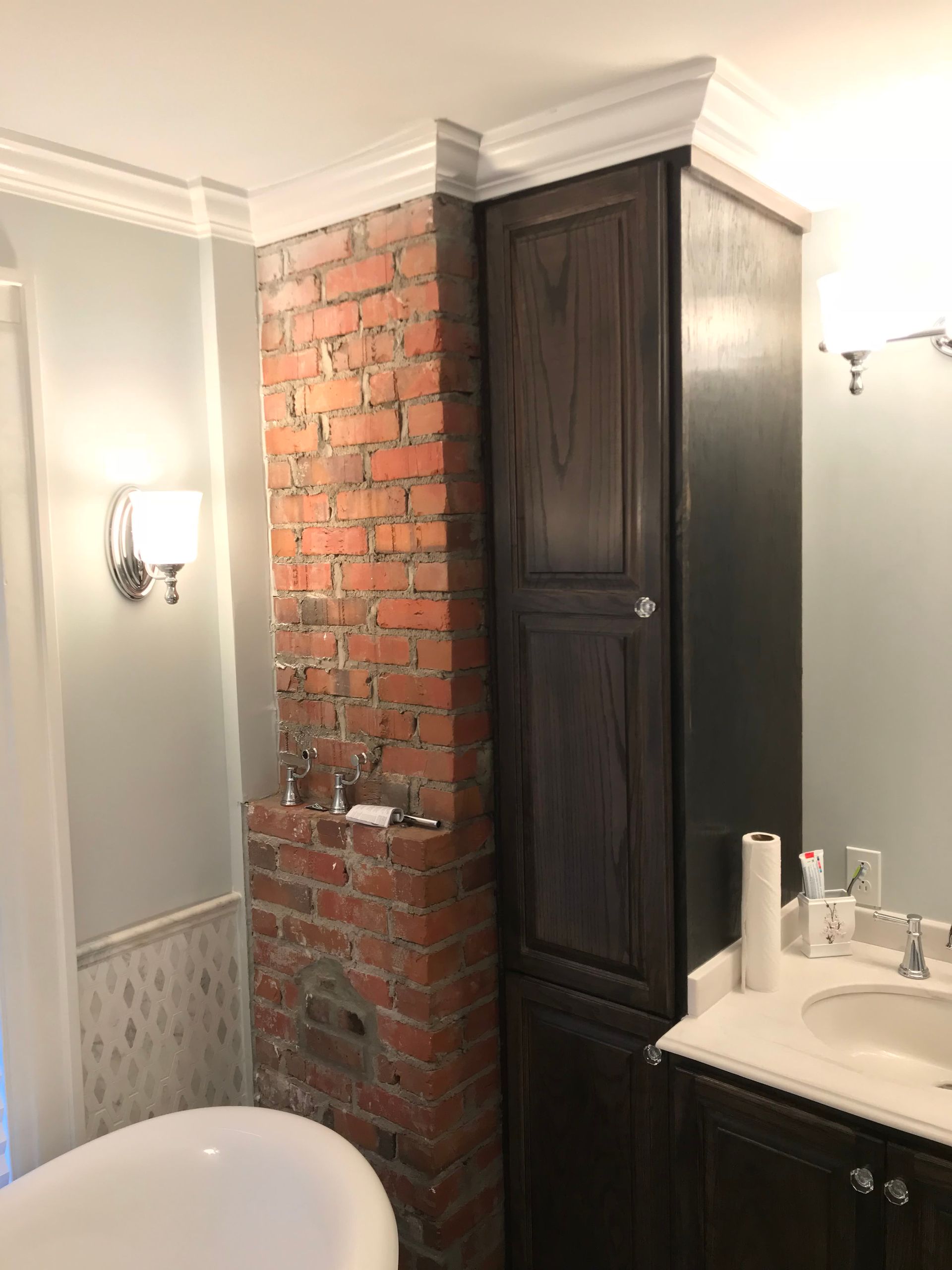 A bathroom with a tub , sink , cabinets and a brick wall.