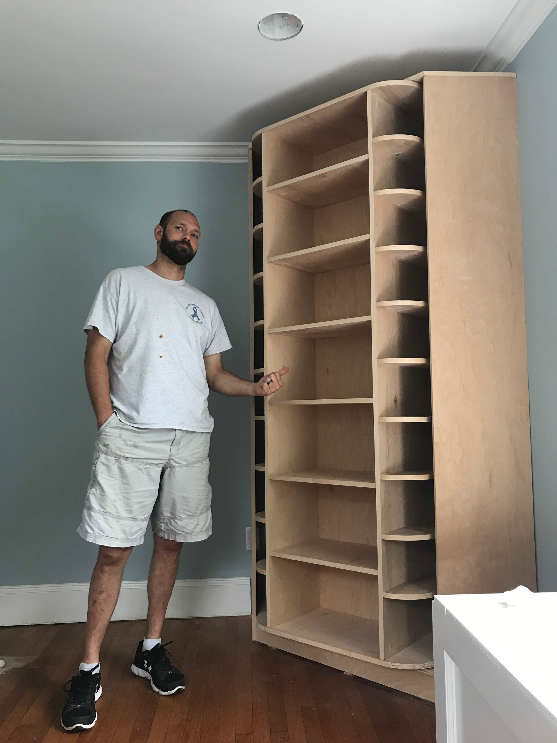 A man is standing next to a large bookshelf in a room.