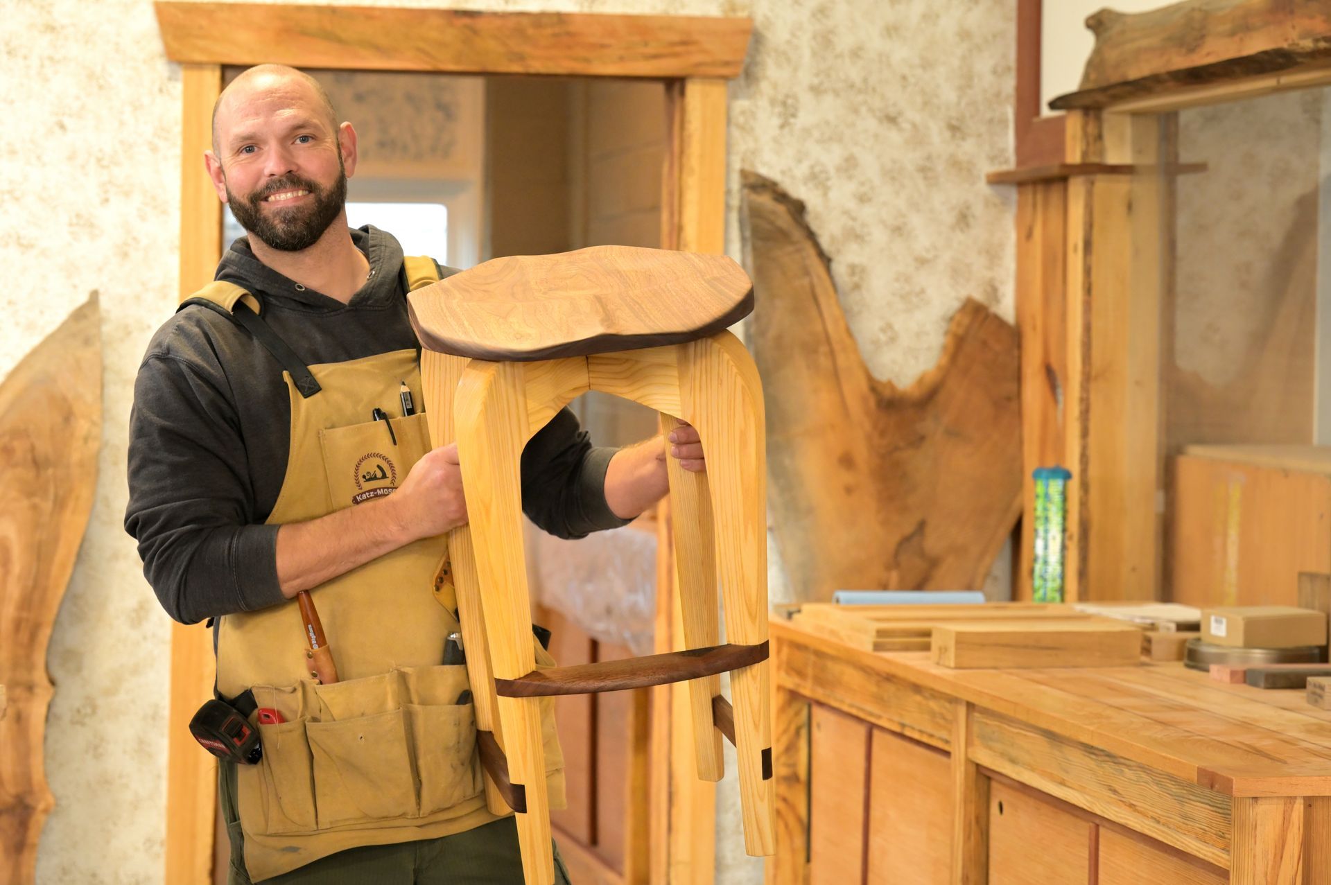 A man is holding a wooden stool in a workshop.