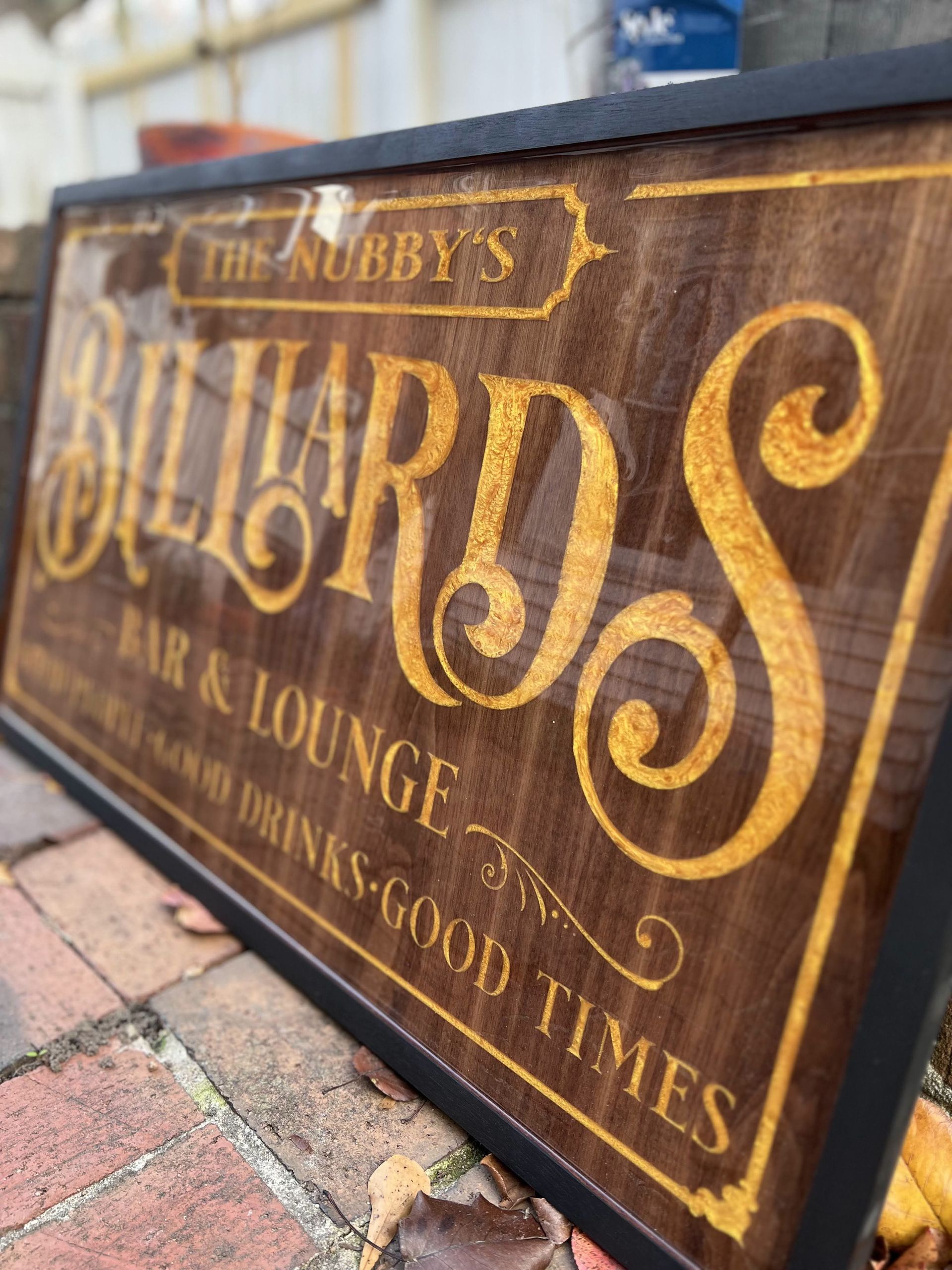 A wooden billiards sign is sitting on a brick sidewalk.
