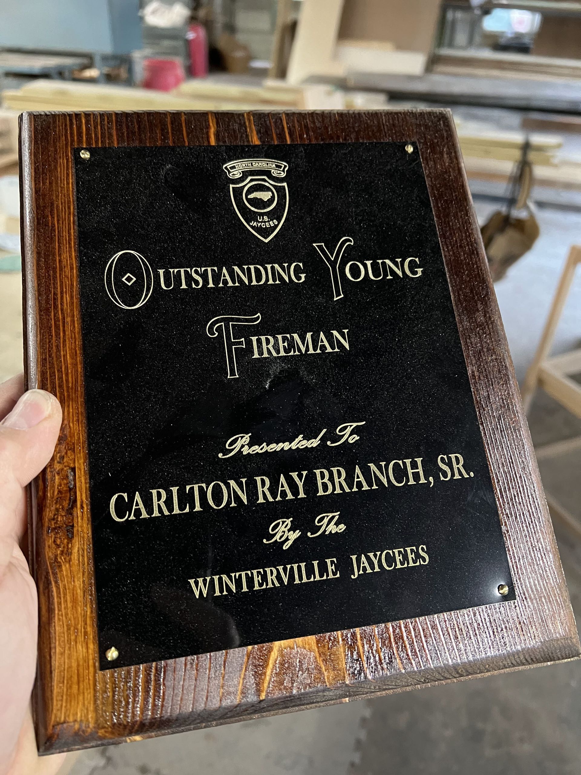 A person is holding a plaque that says ' outstanding young fireman ' on it