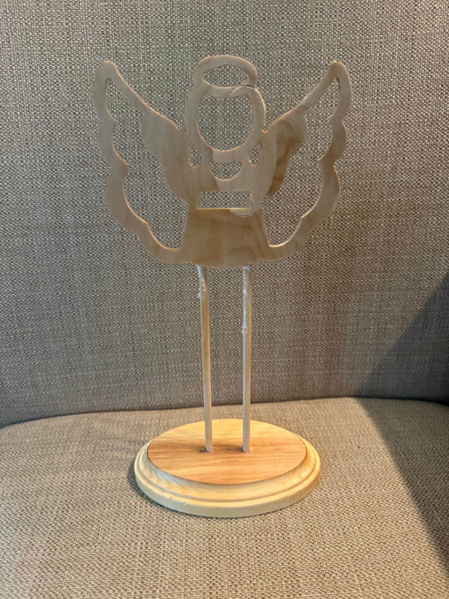 A wooden angel statue is sitting on top of a wooden base on a couch.