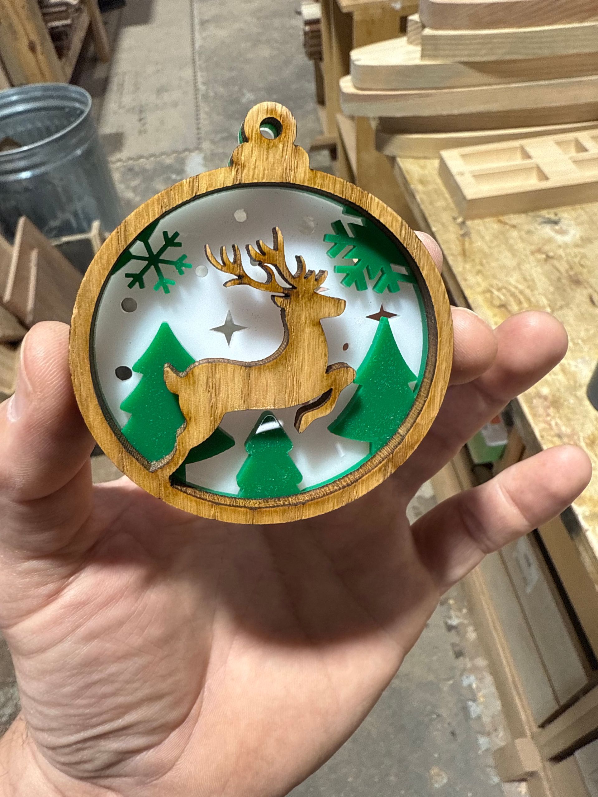 A person is holding a wooden christmas ornament with a deer on it