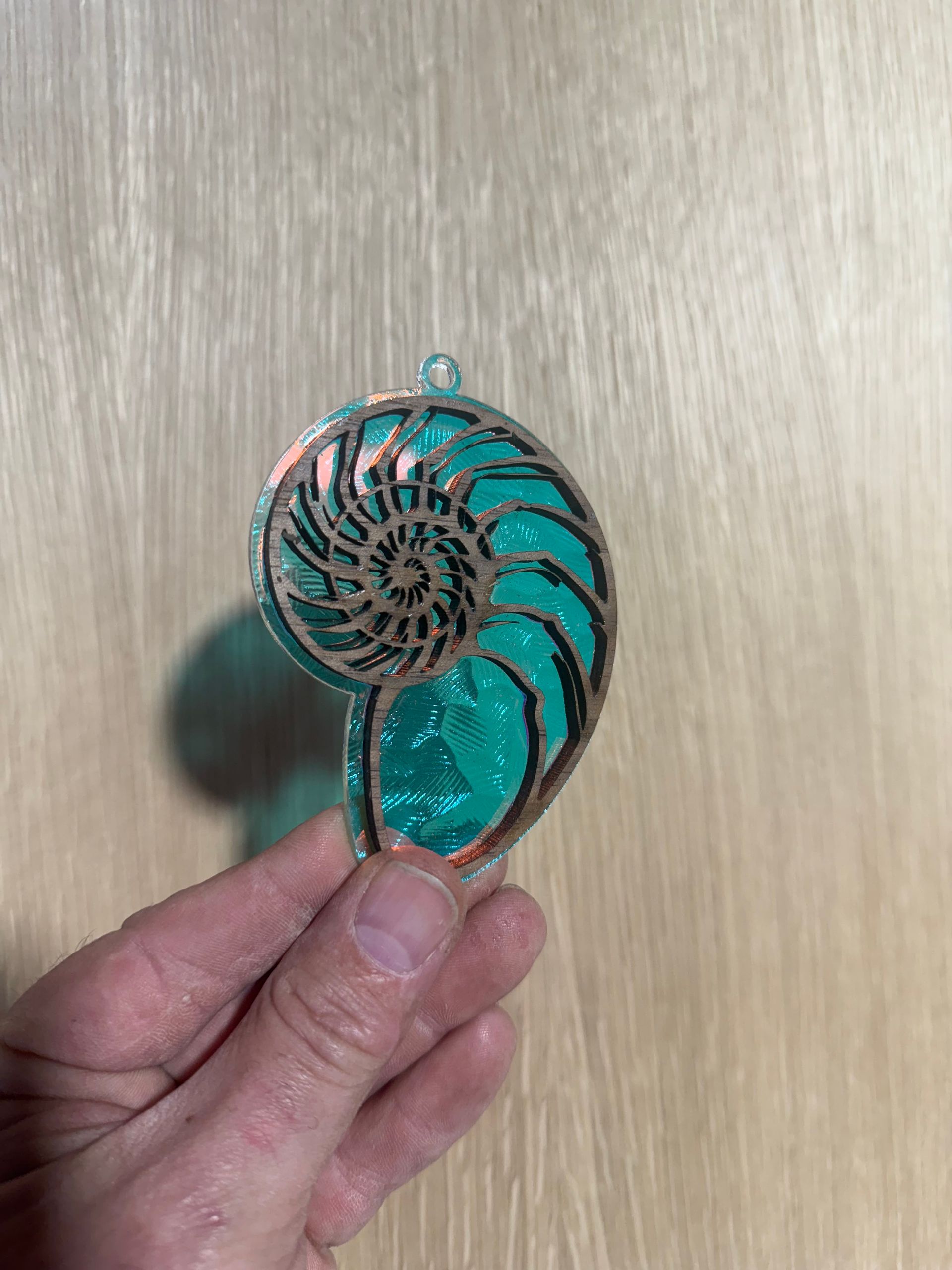 A person is holding a pendant in the shape of a nautilus shell.