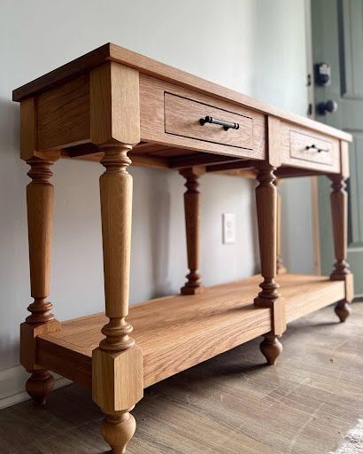 A wooden table with two drawers and a shelf is sitting in a room.