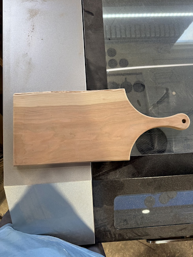 A wooden cutting board with a handle is sitting on top of a stove.
