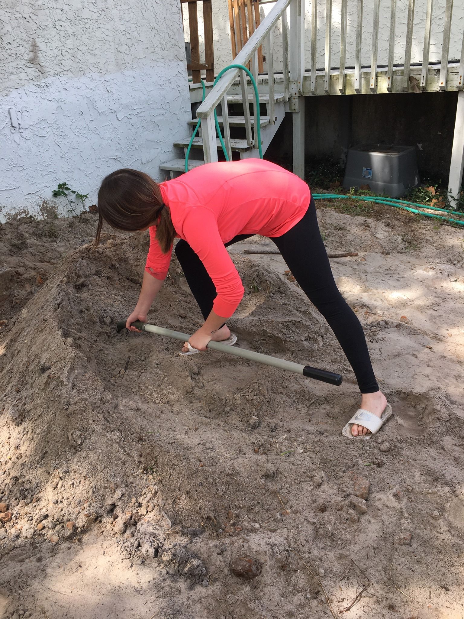 A woman is bending over in the dirt with a shovel.