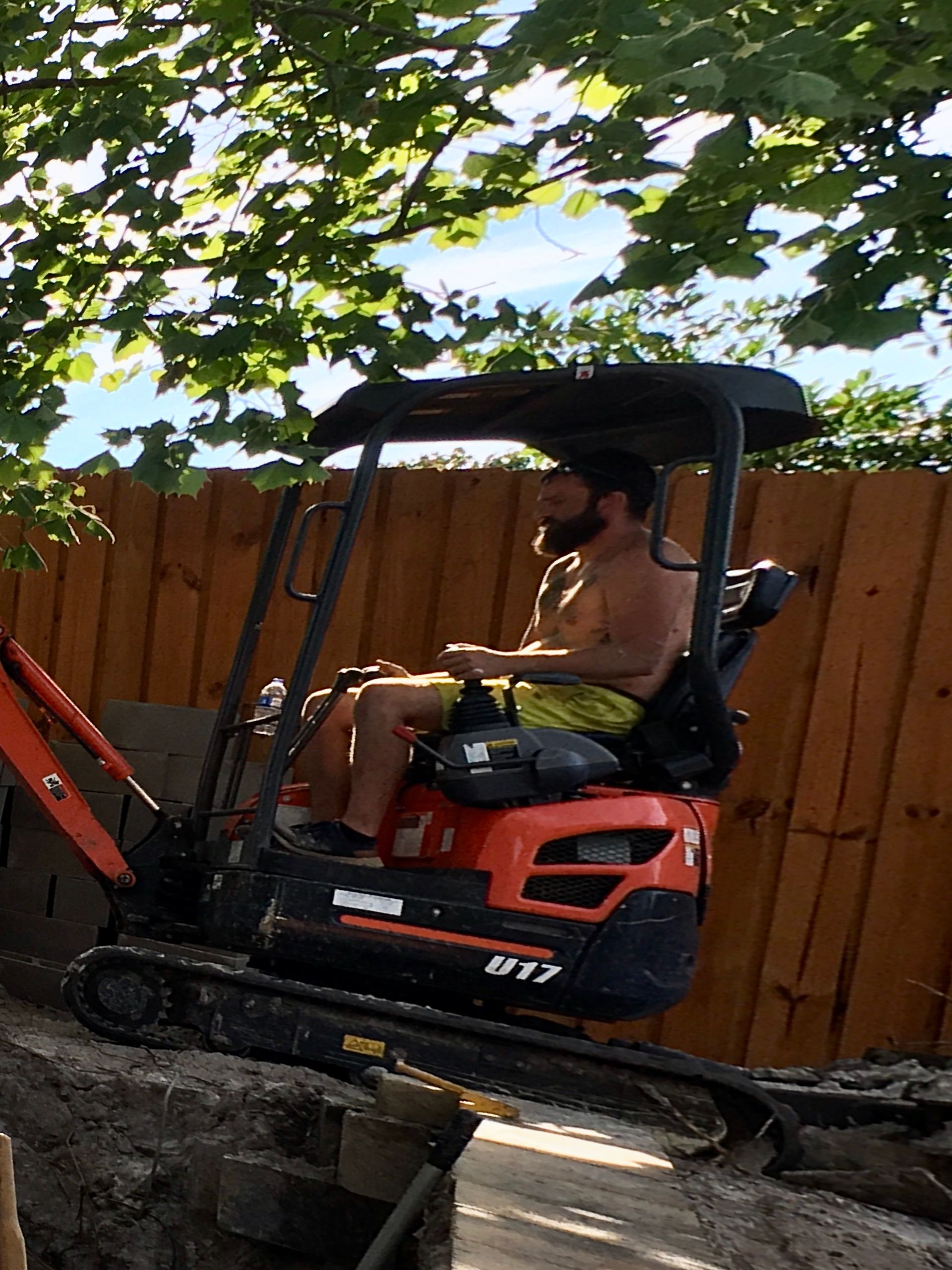 A shirtless man is sitting on a small excavator.