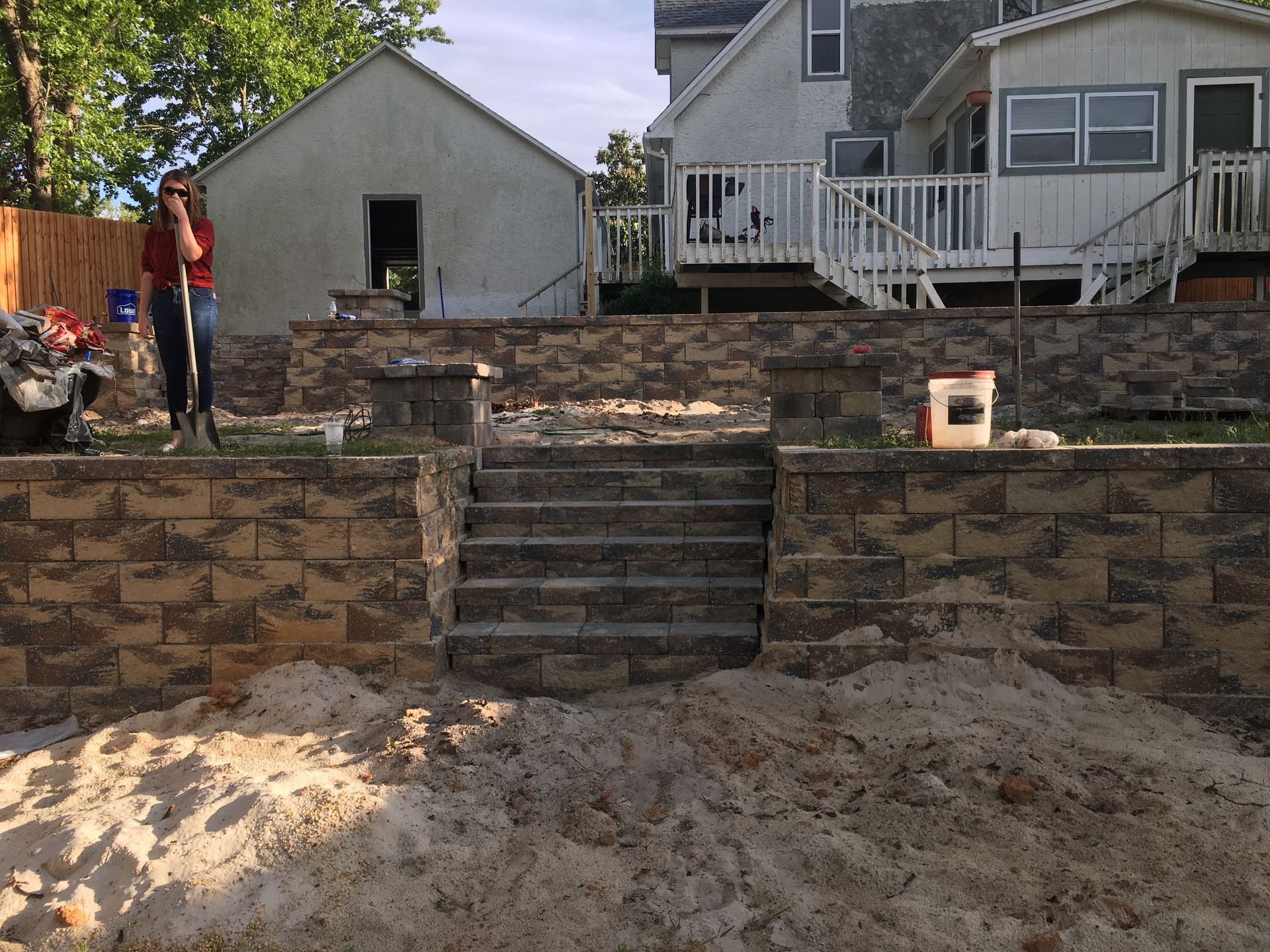 A man is standing in front of a brick wall with stairs and a house in the background