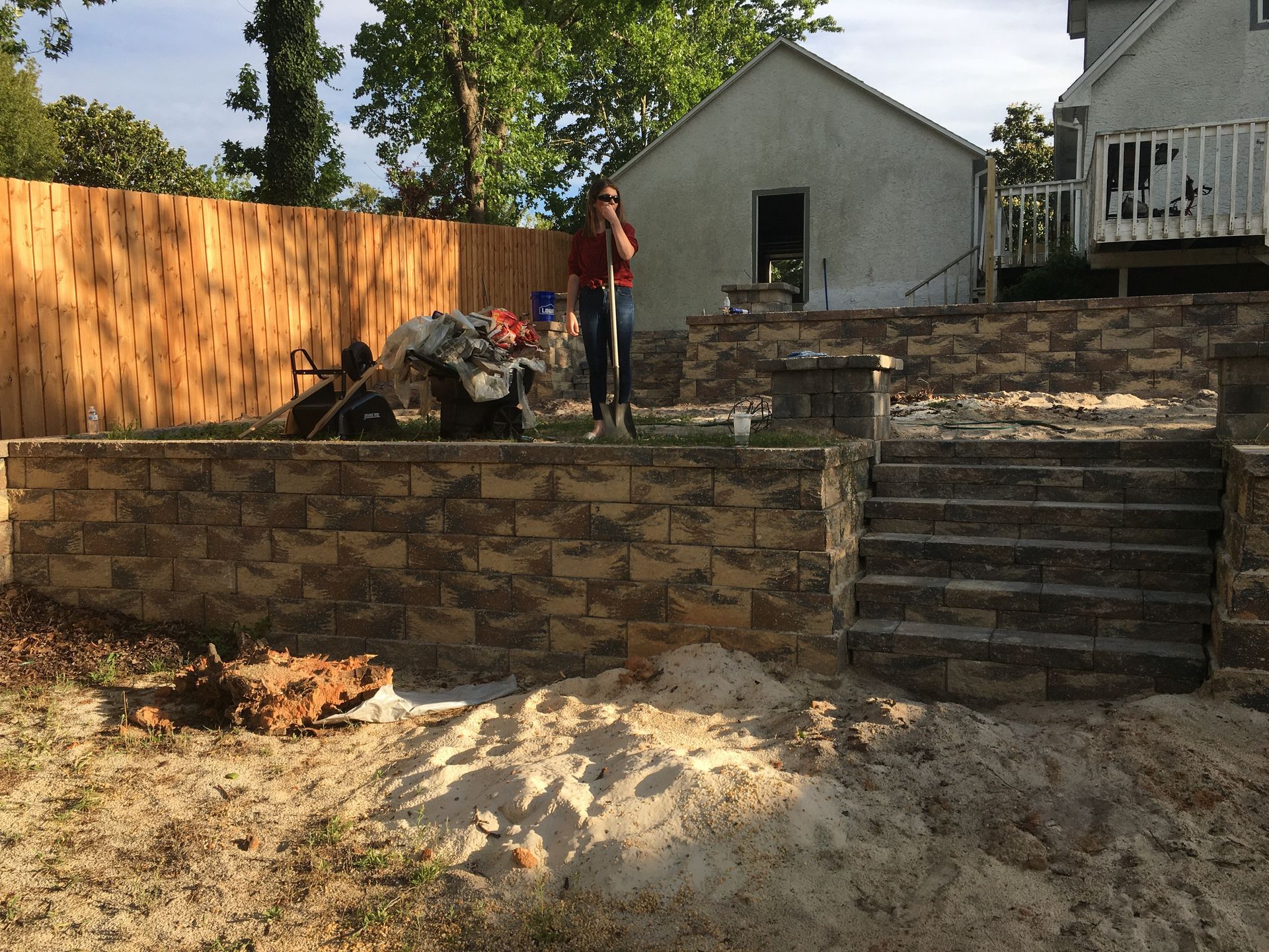 A man is standing in a backyard with a shovel in his hand