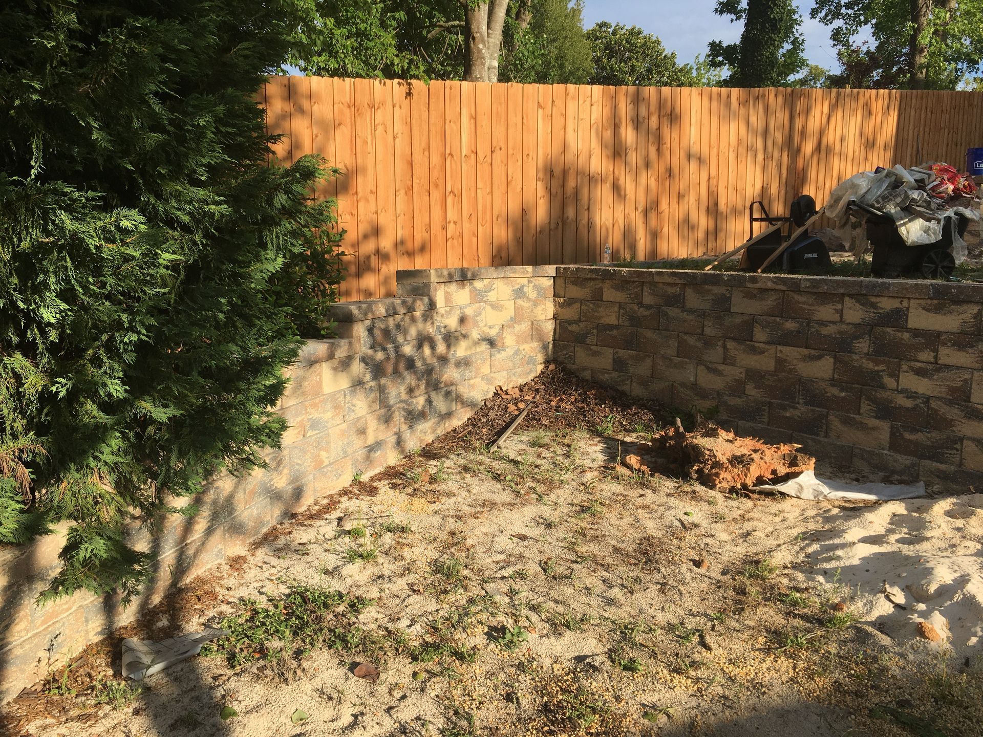 A wooden fence surrounds a stone wall in a backyard.