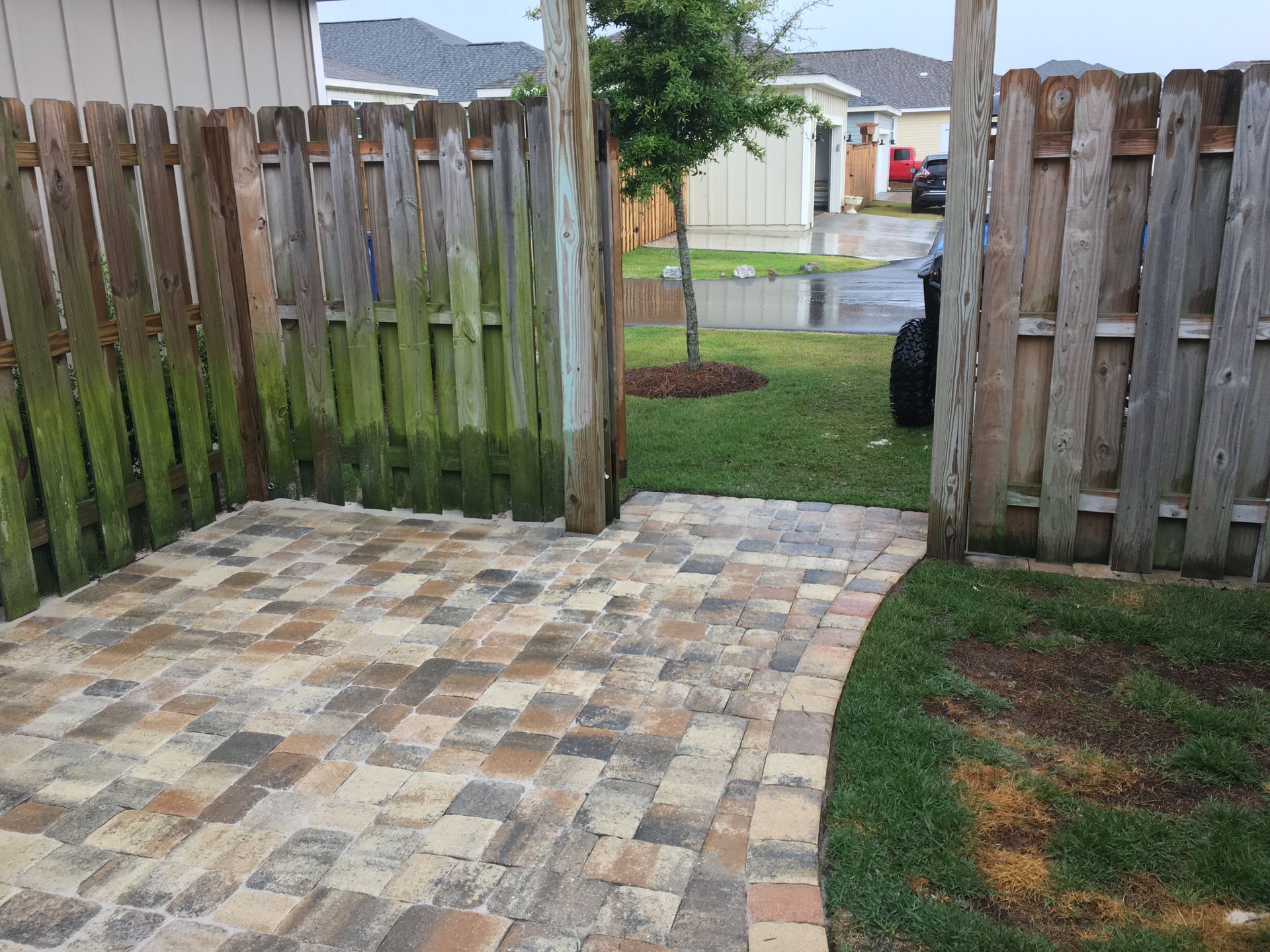 A wooden fence surrounds a brick walkway in a backyard.