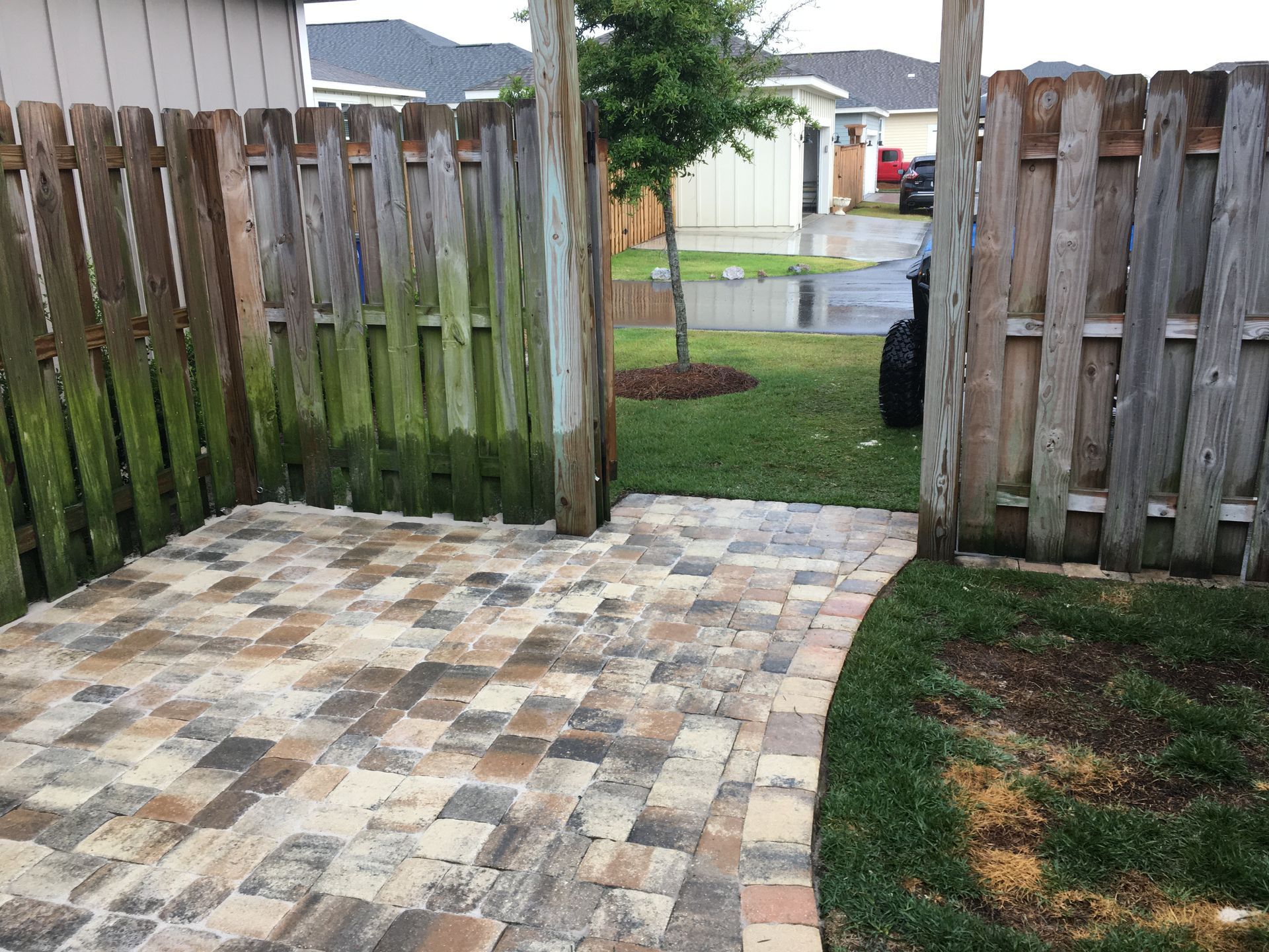 A wooden fence surrounds a brick patio in a backyard.