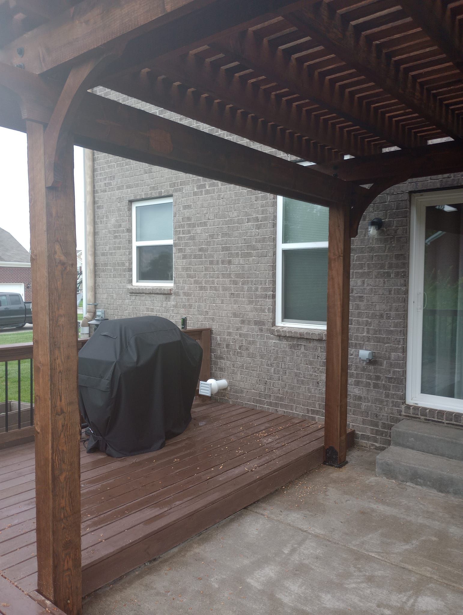 There is a grill on the deck under a pergola.