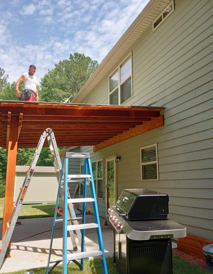 A man is standing on the roof of a house next to a ladder.