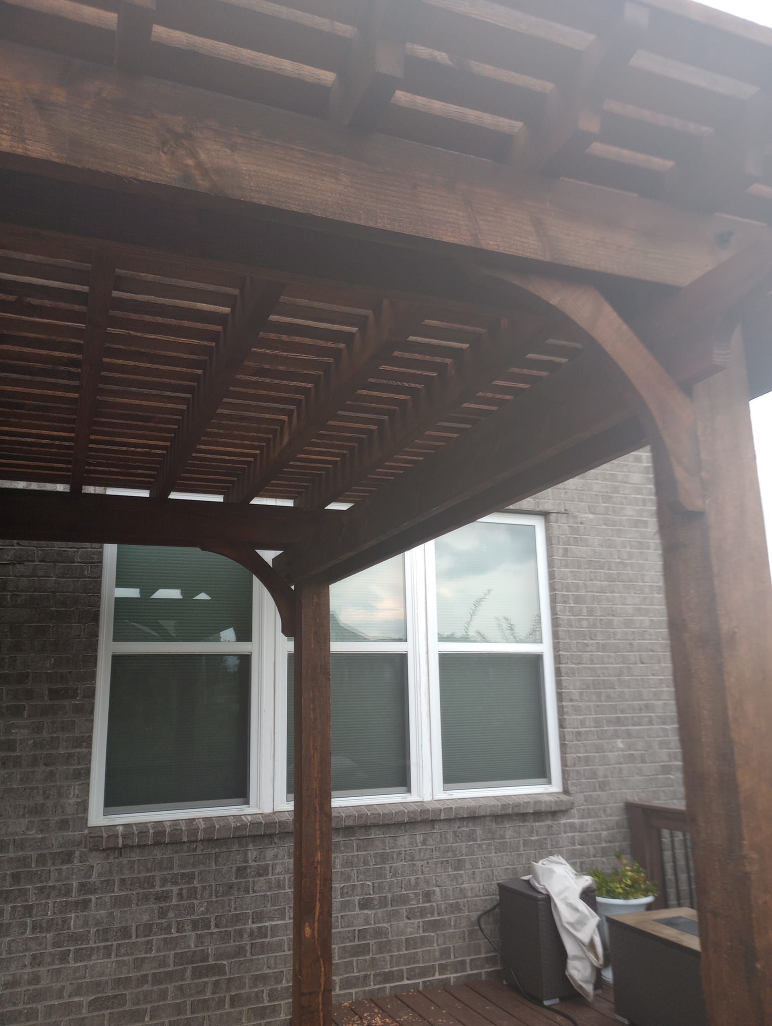 A wooden pergola is sitting on the side of a brick building next to a window.