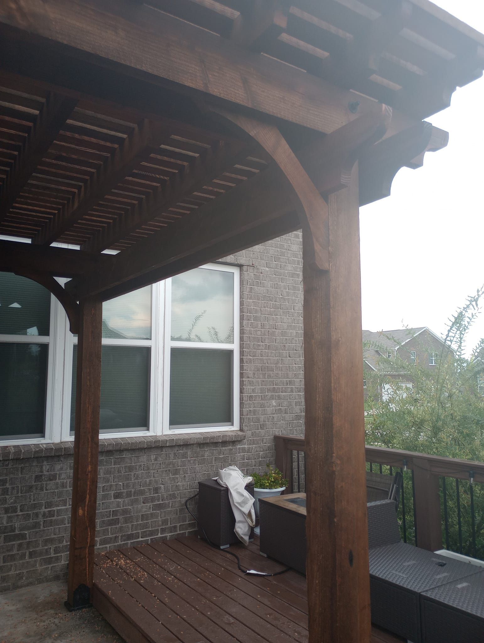 A wooden pergola is sitting on top of a wooden deck next to a brick building.