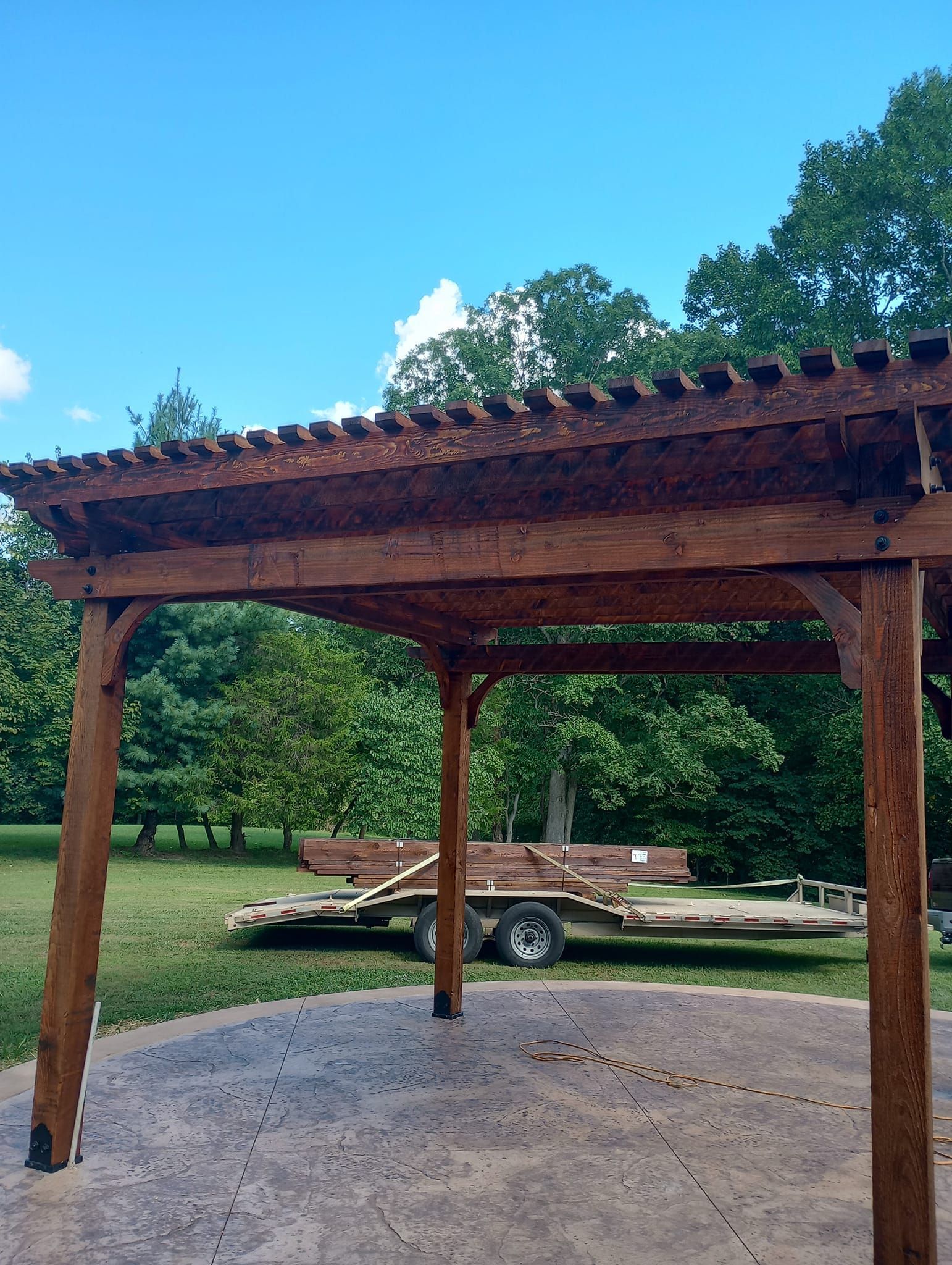 A wooden pergola is sitting on top of a concrete patio next to a trailer.