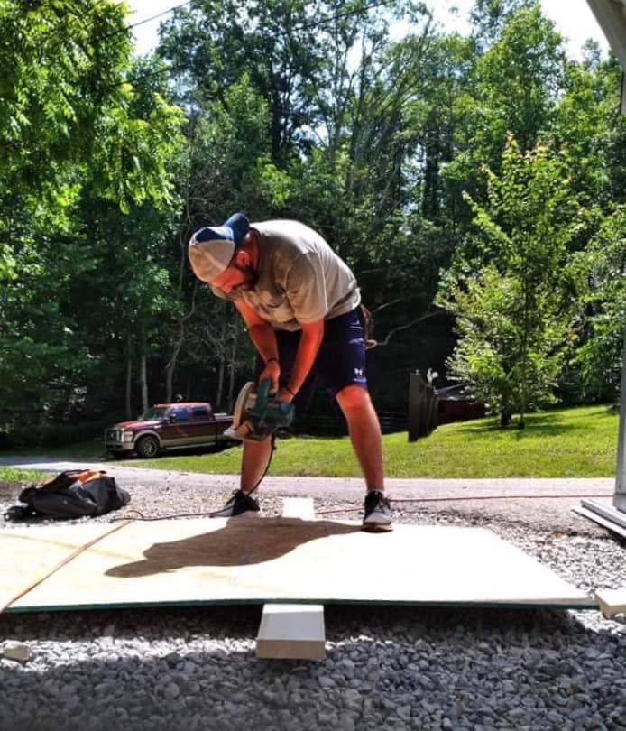 A man is using a saw to cut a piece of plywood