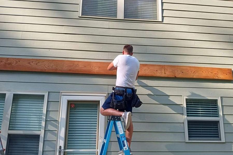 A man on a ladder is working on the side of a house