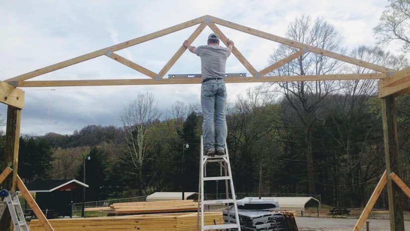 A man is standing on a ladder working on a wooden structure.