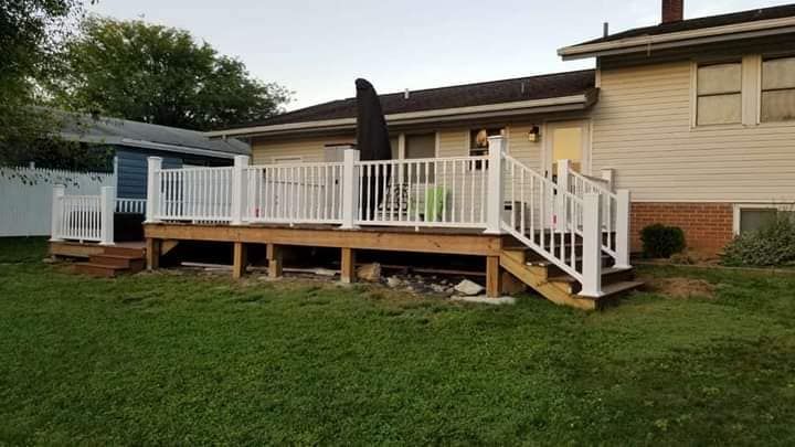 A large deck with stairs and a white railing is in the backyard of a house.