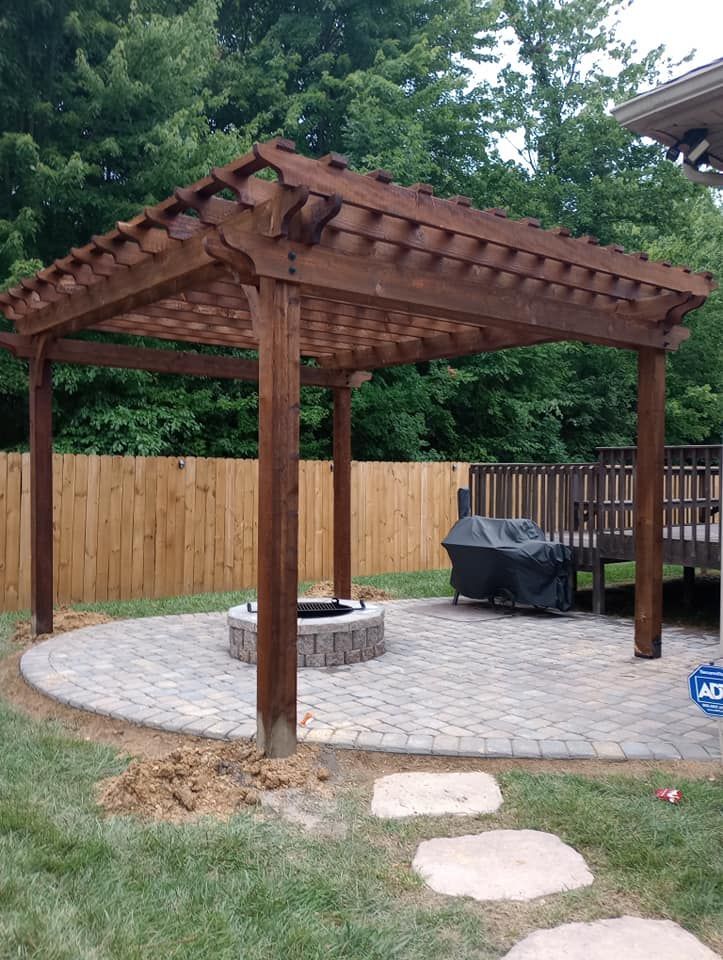 There is a fire pit under a pergola in the backyard.