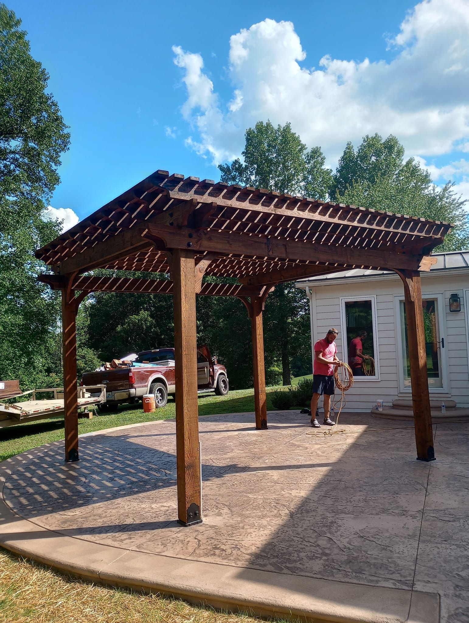A man is standing under a wooden pergola in front of a house.