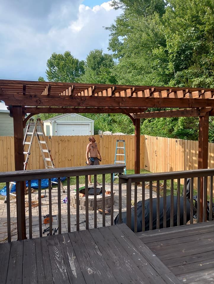 A man is standing under a wooden pergola on a deck.