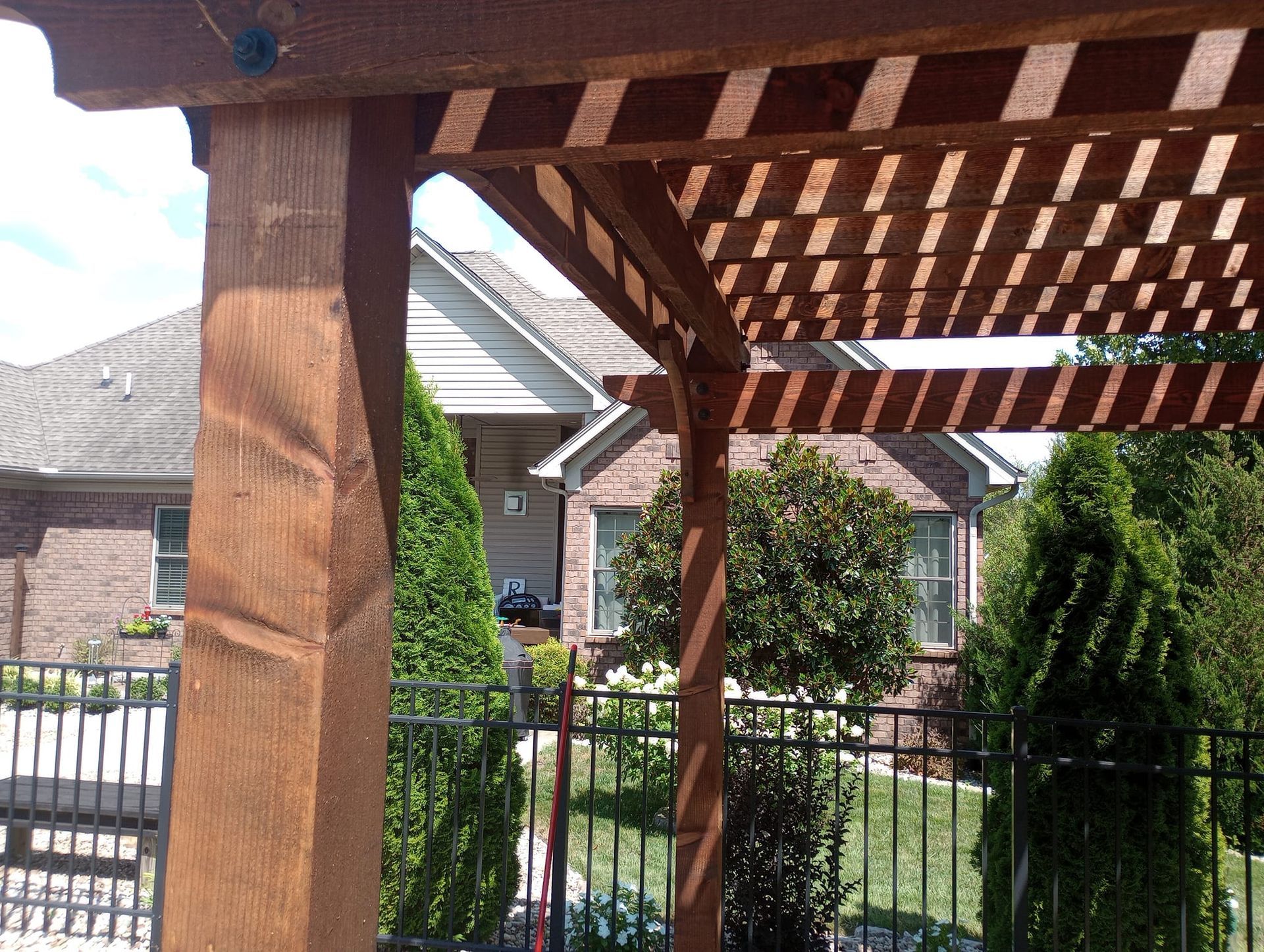 A wooden pergola in a backyard with a house in the background