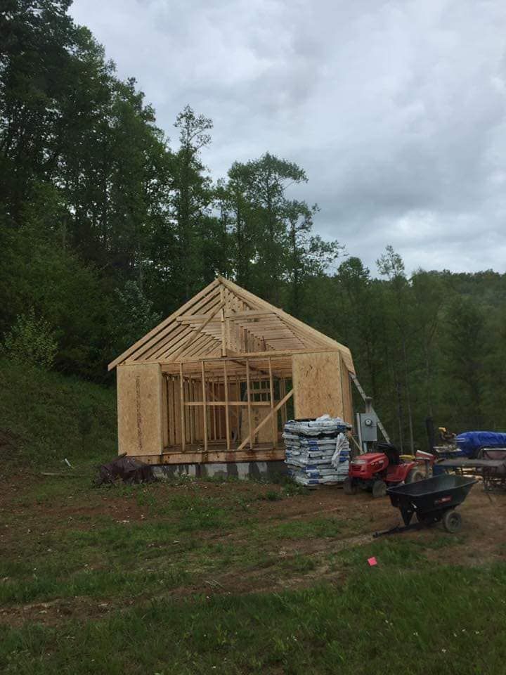 A wooden house is being built in a field with trees in the background.