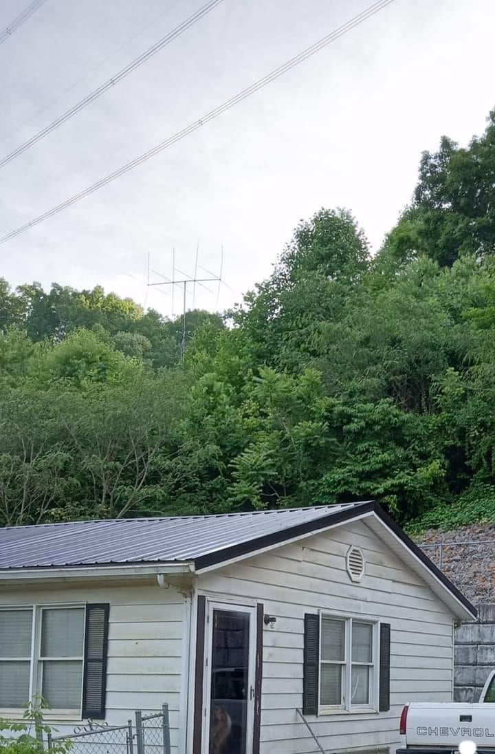 A small white house with a truck parked in front of it surrounded by trees.
