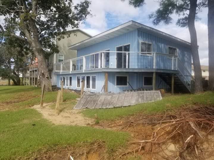 A blue house with a large deck is sitting on top of a grassy hill.